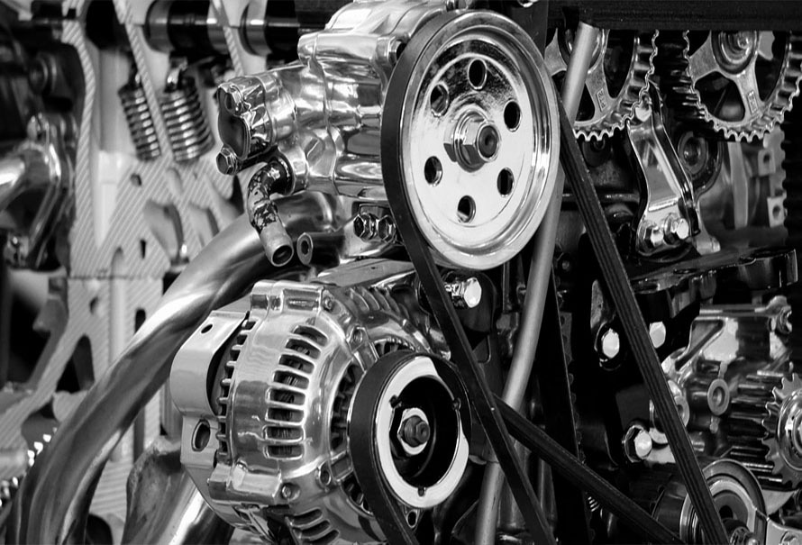 Black-and-white close-up of a polished car engine with pulleys, belts, and camshaft gears