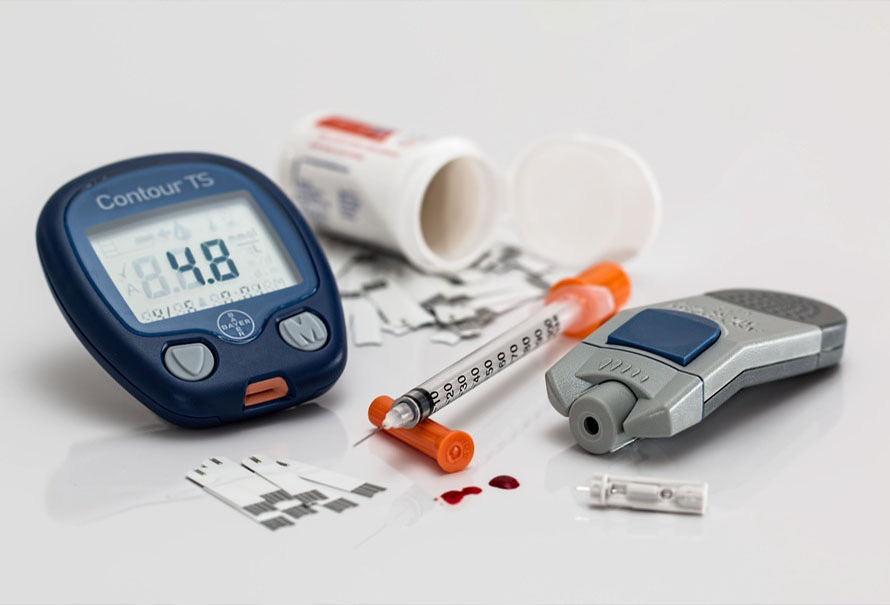 Diabetes care supplies: a blood glucose meter showing a reading, test strips, a syringe, and a lancing device