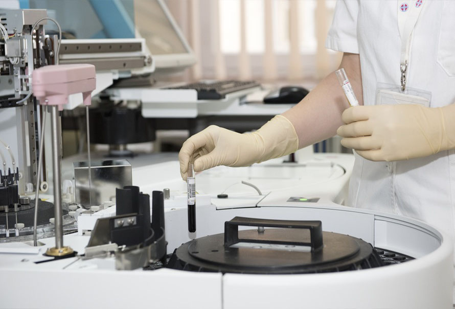 Gloved hands of a laboratory technician loading sample vials into an automated analyzer