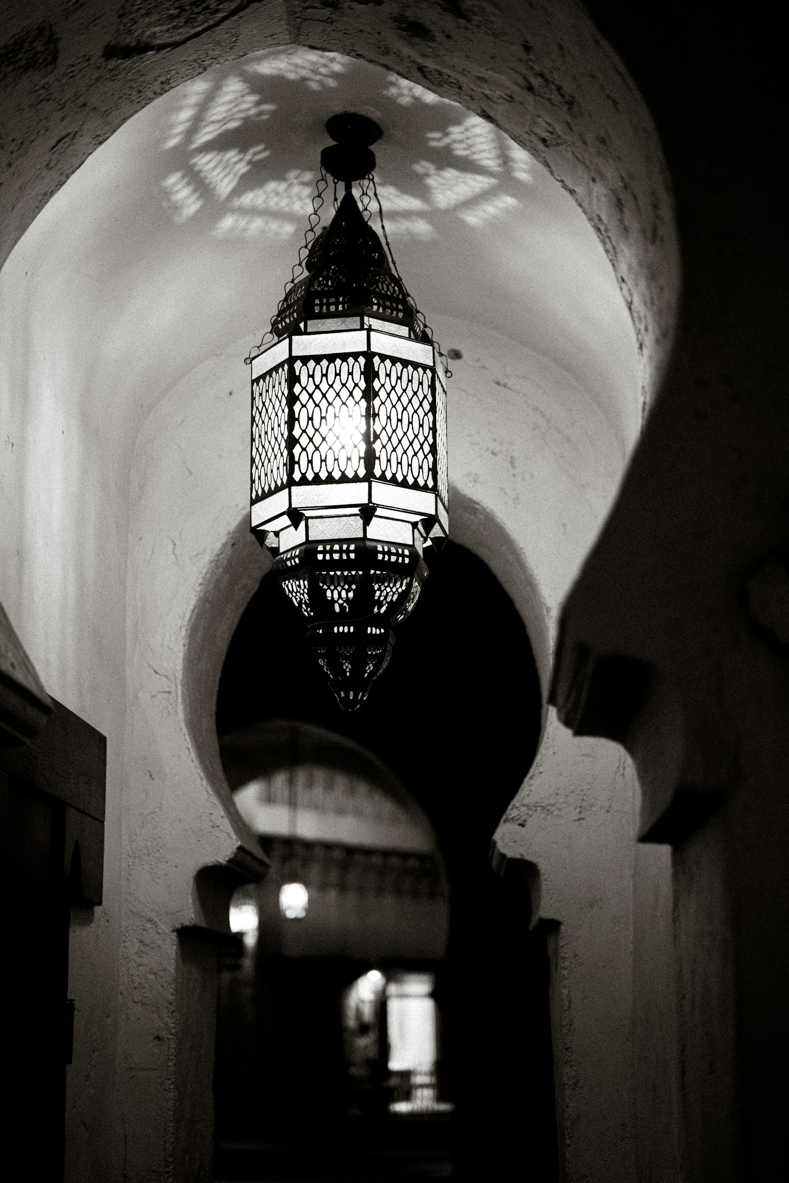 Arched stone corridor lit by warm hanging oil lamps